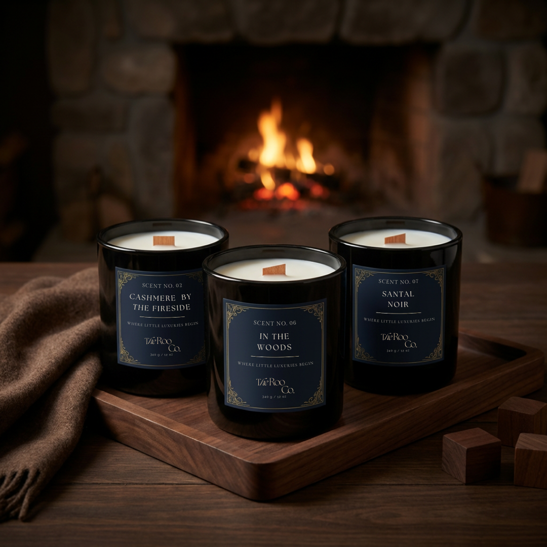 Woody candle collection by The Roo Co featuring Cashmere by the Fireside, In the Woods, and Santal Noir, styled on a wooden tray by a lit fireplace for a warm, cozy ambiance.