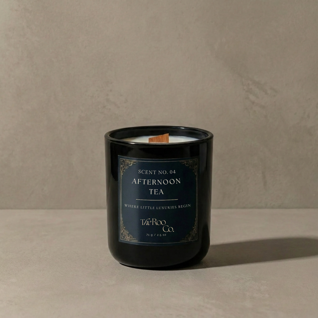 A black glass jar candle with a dark blue label reading 'Scent No. 04 afternoon tea by the roo co