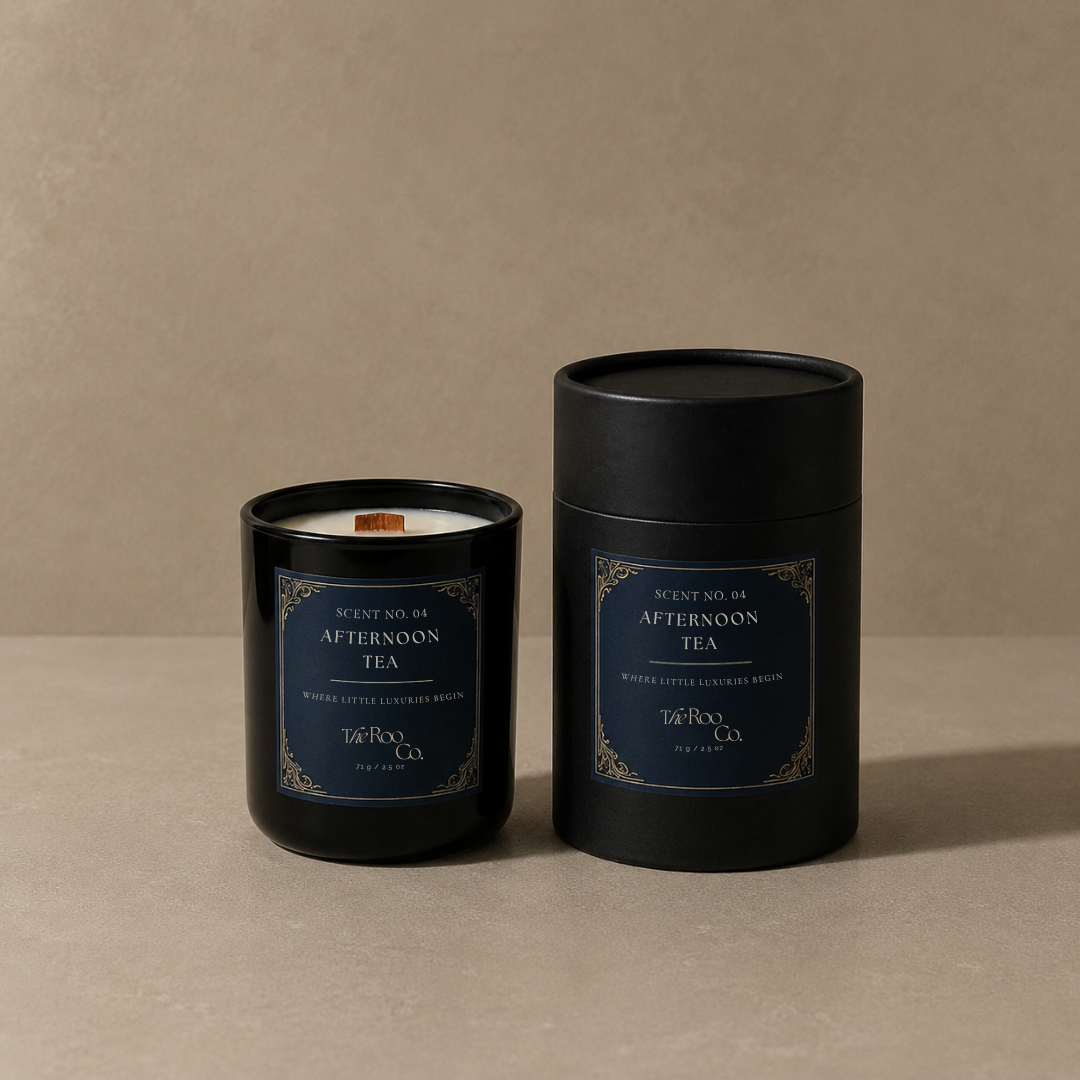 A black glass jar candle and its matching black cylindrical container, both labeled afternoon tea' by the roo co., set against a warm beige textured background.