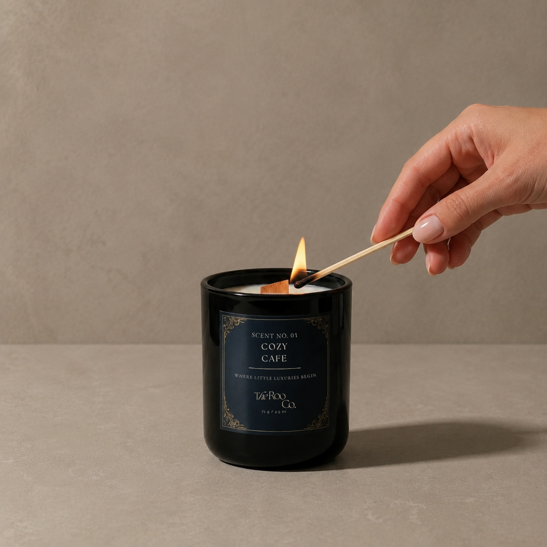 Cozy Café luxury coconut soy candle in a glossy black glass jar with a wooden wick on a neutral beige background with hand lighting a candle